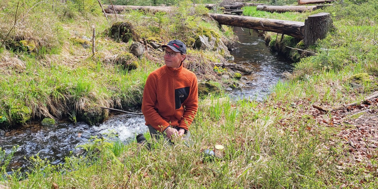 Jürgen Franz Oswald kniet neben einem Bachlauf in Maut, Bayern